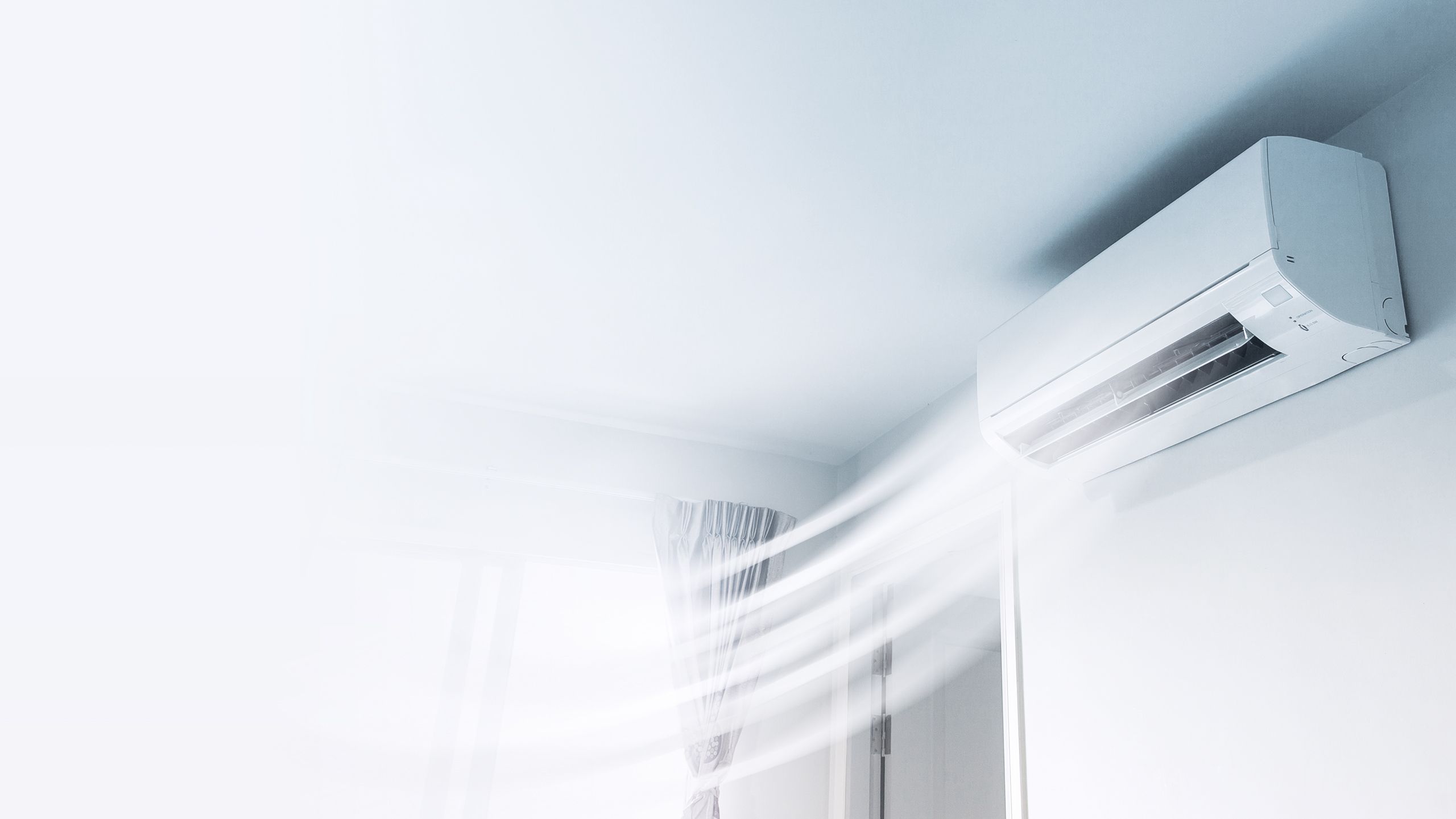 Eine Klimaanlage an einer weißen Wand bläst kühle Luft in einem Raum mit einem Fenster im Hintergrund.